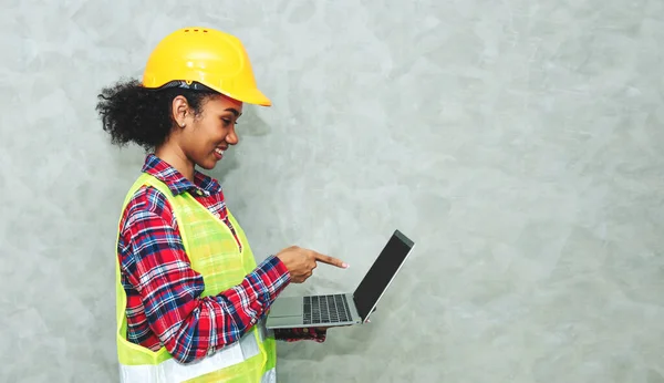 Portrait of professional young black woman civil engineer , architecture worker wearing hard hat safety for working in construction site or warehouse,using laptop for work.