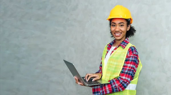 Portrait of professional young black woman civil engineer , architecture worker wearing hard hat safety for working in construction site or warehouse,using laptop for work.