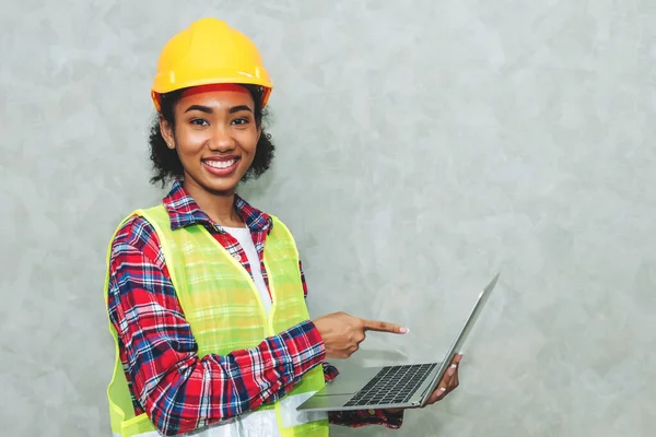 Portrait of professional young black woman civil engineer , architecture worker wearing hard hat safety for working in construction site or warehouse,using laptop for work.