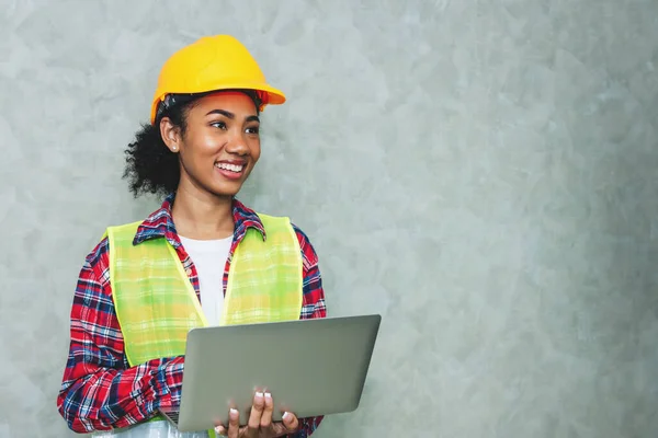 Portrait of professional young black woman civil engineer , architecture worker wearing hard hat safety for working in construction site or warehouse,using laptop for work.