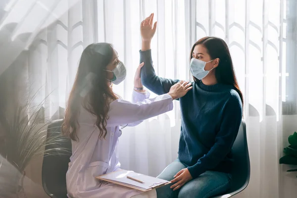 Asian doctor visit and examines on young adult woman at hospital with office syndrome symptom.The doctor checking up and consulting for health care, wearing a mask to protect covid-19 pandemic