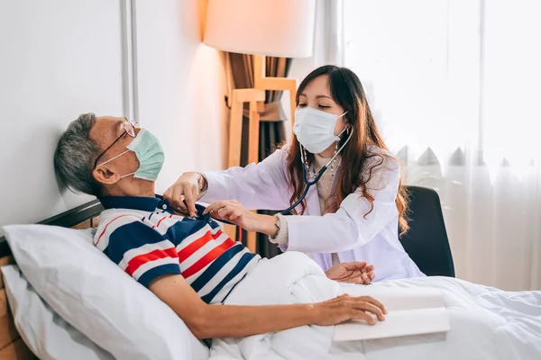 Asian doctor using a stethoscope to examines a senior man at home ,The doctor checking up and consulting for retirement health partient,hospital services ,and wearing a mask to protect covid-19.