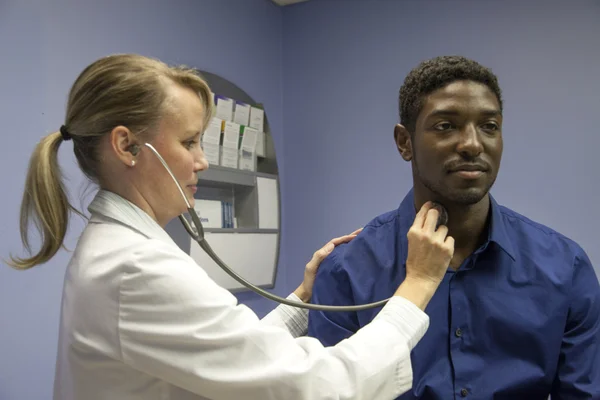 Beyaz kadın doktor inceler ve Afro-Amerikan erkek fiziksel verir — Stok fotoğraf