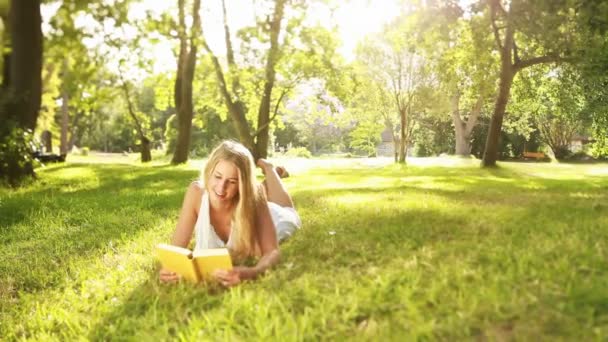 Женщина улыбается с книгой в саду — стоковое видео