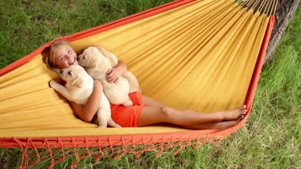 Happy girl holding labrador puppies while swinging in hammock — Stock Video