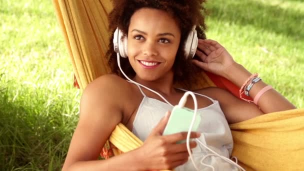Женщина лежит в гамаке и слушает музыку в наушниках — стоковое видео