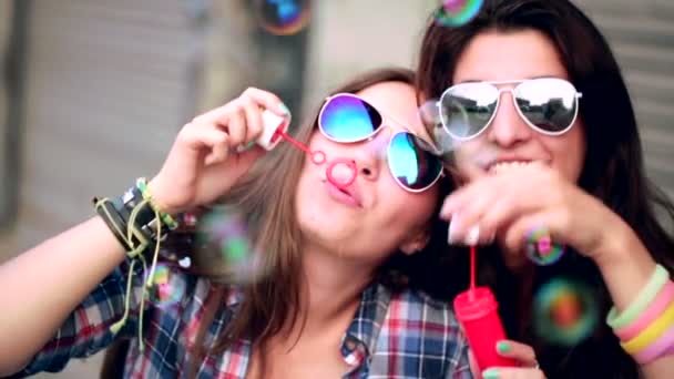 Девушки в солнечных очках веселятся делая пузыри — стоковое видео