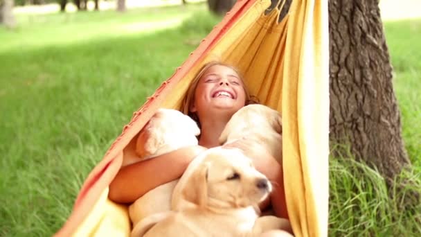 Menina feliz segurando filhotes labrador enquanto balançando na rede — Vídeo de Stock