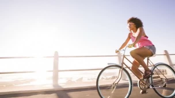 Chica montando una bicicleta cerca del océano — Vídeos de Stock