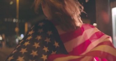 Genç bir kadının omuzları üzerinde şehir geceleri sokak sokak ışıkları bayrak gölgeler parlayan ile tek başına çalışan üzerinde bol dökümlü bir Amerikan bayrağı ile dikiz