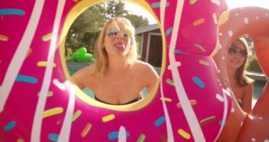 Dört kız bir havuz yanında oturan ve komik havuzu Powerboats tutan arkadaşlar videonun kaydırma donuts ve mutlu bir şekilde kameraya gülümseyen açık havada bir yaz gününde çubuk kraker, gibi görünmek için yapılmış