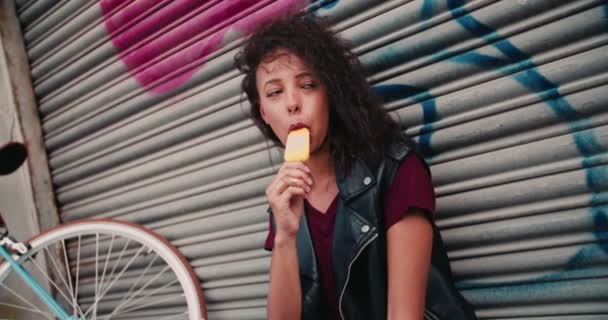 スローモーションでアイス キャンデーを食べる彼女の自転車の都市歩道の上に座って 代のアフリカ系アメリカ人少女 — ストック動画