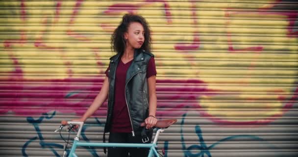 Adolescente Afroamericana Pie Una Acera Frente Graffitti Urbano Con Bicicleta — Vídeos de Stock