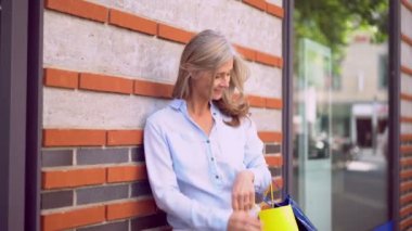 Gri saçlı Olgun kadın bir butik şehir pencerenin yanında dururken gülümseyen