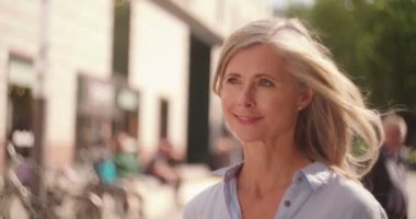 Güvenle bir şehir alışveriş torbaları tutarken sokak aşağı yürüyüş gri saçlı Olgun kadın gülümseyerek