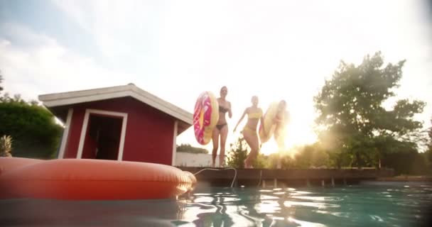 三个女孩半空中同时按住大游泳池充气并在夏天的晚上 与太阳耀斑在慢动作中快乐地跳进后院的游泳池 — 图库视频影像