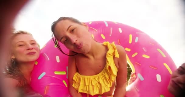 三个女孩带看上去像大的粉色甜甜圈玩 一边对着镜头在一个夏日的午后 在一个后院 Sunflare 上接吻鬼脸游泳池充气浮在游泳池里 — 图库视频影像