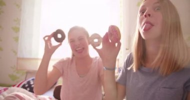 Saçma ve yeme renkli donuts onların pijama giyen süre varlık birlikte güneşli bir yatak odasında gülen iki genç kız