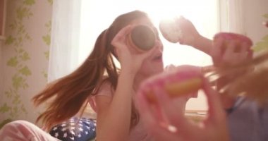 Genç kızlar bir eğlenirken gözleri kadar renkli donut tutan pijama partisi güneşli bir yatak odasında