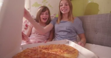 İki genç kız gülümseyerek mutlu bir pijama partisi ve onların pijama içinde dışarı asılı iken büyük boy pizza içeren bir paket kutusu açılıyor