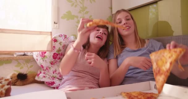 青春期的女孩朋友年龄每在床上 穿着睡衣在家吃一块巨大的披萨 — 图库视频影像