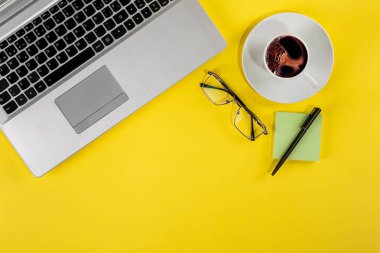 Bir dizüstü bilgisayarın, bir fincan kahvenin ve sarı arkaplandaki sabit elementlerin en iyi görüntü stüdyo fotoğrafı.