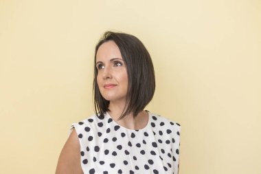 Polka noktalı kıyafet giyen İspanyol kadın stüdyoda bej arka plana bakıyor.