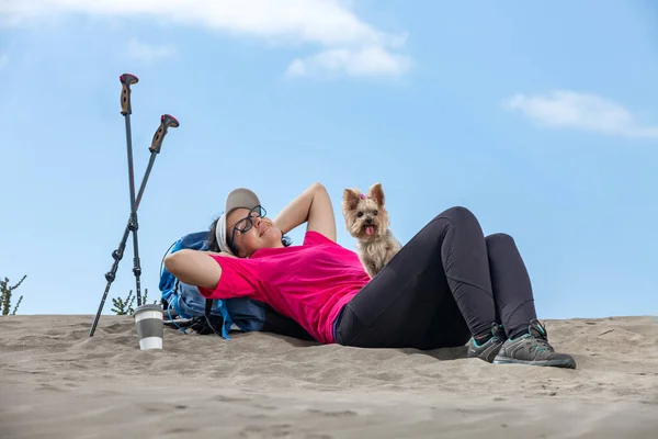Low angle of female explorer lying on backpack on Famara coast with cute dog and taking break during hike