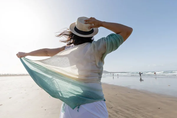 在靠近大海的沙滩上度过一个多风的周末 带着薄围巾 触摸草帽 享受自由的黑发女孩的背影 — 图库照片