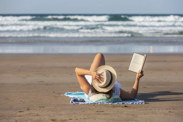 Anonymous Woman Touching Hat Reading Book While Lying Sand Waving — Stock Photo, Image