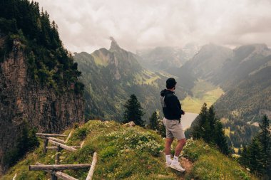 Bir adam güzel bir yürüyüşten sonra bir dağın tepesinde durur ve doğaya hayran kalır.