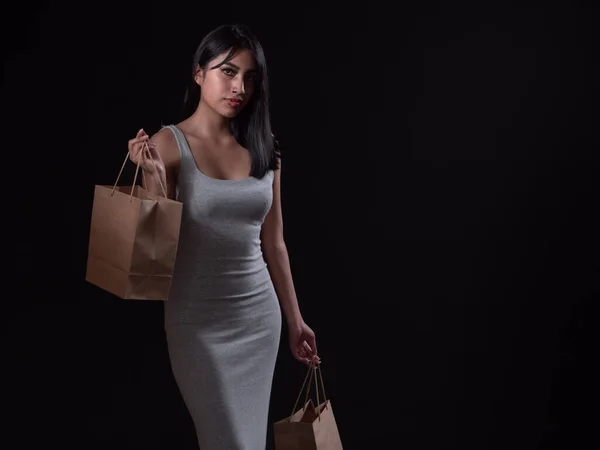 Hispanic girl with eco-friendly cardboard bags isolated on black background, shopping concept