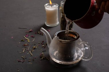 Çay demliğinin yan görünüşü, siyah zemine sıcak su eklenmesi, meditasyon için çay hazırlama kavramı..