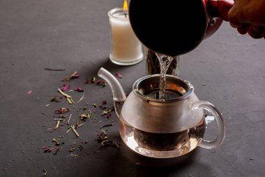 Çay eşliğinde çaydanlığın yan görünüşü, siyah zemine sıcak su eklenmesi, rahatlamanıza yardımcı olması için çay hazırlama kavramı