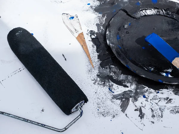 painter's accessories, container with black paint, piece of wood with blue paint, roller and palette knife on a white background