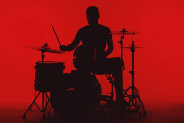 Silhouette of a young man playing drums on a red background.
