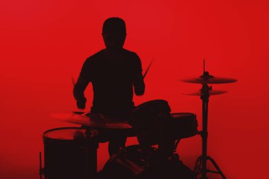 Silhouette of a young man playing drums on a red background.