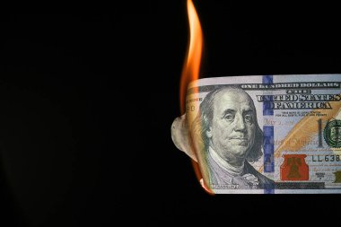 Siyah arka planda yanan 100 dolarlık banknotun yakın plan çekimi..