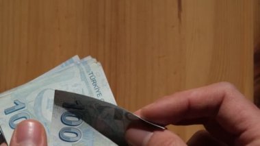 Tahta bir arka planda 100 Türk lirası banknot saymak.