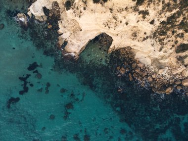 Mavi renkli denizi ve sarı kayaları olan kayalık bir sahilin havadan görünüşü..