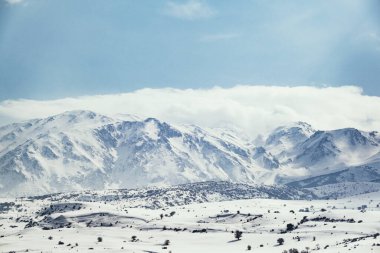 Karlı ve bulutlu bir dağın manzarası.