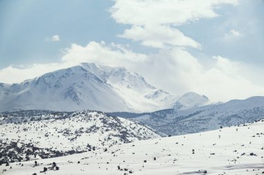 Karlı ve bulutlu bir dağın manzarası.