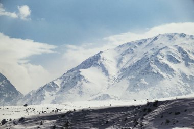 Karlı ve bulutlu bir dağın manzarası.