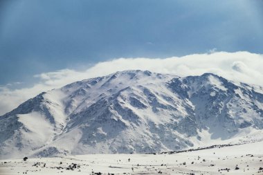 Karlı ve bulutlu bir dağın manzarası.