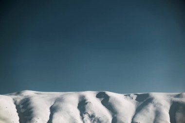 Karlı ve mavi gökyüzü olan dağların manzarası.