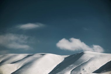 Karlı, mavi gökyüzü ve bulutlu bir dağın manzarası..