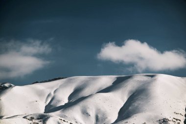 Karlı, mavi gökyüzü ve bulutlu bir dağın manzarası..