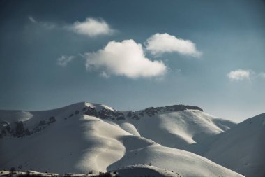 Karlı, mavi gökyüzü ve bulutlu bir dağın manzara manzarası.