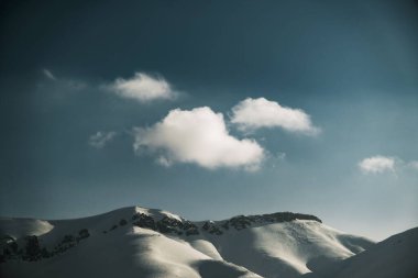 Karlı, mavi gökyüzü ve bulutlu bir dağın manzarası..