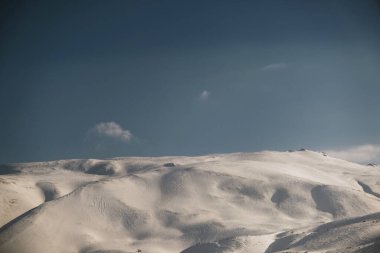 Karlı, mavi gökyüzü ve bulutlu bir dağın manzarası..